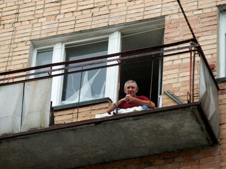 Мужчина сидит возле разбитого взрывной волной стекла на балконе своей квартиры в поселке Нагорный Самарской области. Фото: РИА Новости