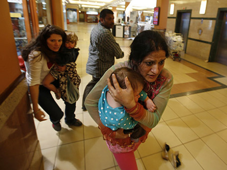 Женщины с детьми выбегают из торгового центра, захваченного террористами, в то время как вооруженный полицейский (на втором плане) следит за обстановкой. Найроби, Кения. Фото: Reuters