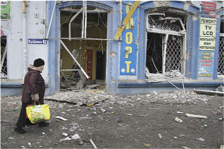 Женщина проходит мимо обстрелянного здания рядом с автобусной остановкой в Донецке