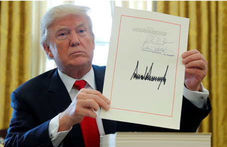 Американский президент Дональд Трамп демонстрирует подписанный закон о налоговой реформе.
