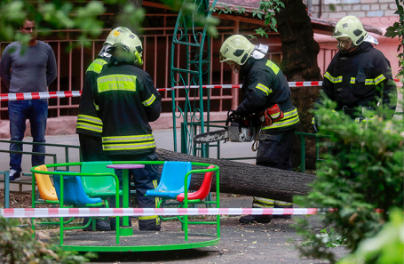 Сотрудники пожарно-спасательной службы распиливают дерево на детской площадке во дворе жилого дома в Гольяновском проезде, которое из-за порывов ветра упало на ребенка.