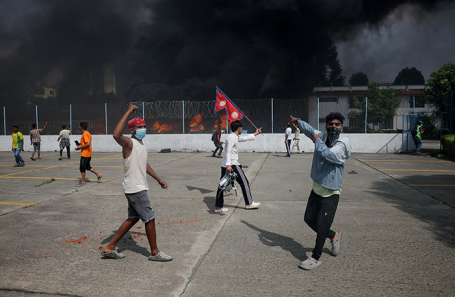 Протестующие на фоне дыма, поднимающегося из здания парламента в ходе антикоррупционных протестов в Катманду.