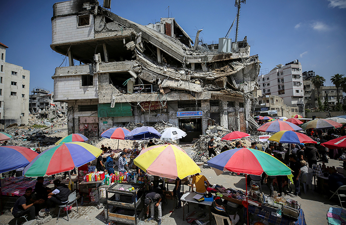Палестинские уличные торговцы продают товары возле разрушенного здания, в котором размещался Банк Иордании, в городе Газа.