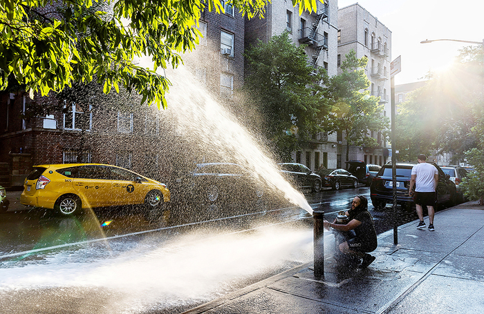 Мужчина охлаждается около открытого гидранта с водой в жаркий день в Бронксе, Нью-Йорк, США.