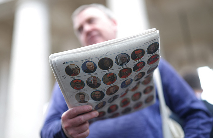 Мужчина у собора Святого Петра в Ватикане держит газету с портретами кардиналов. Конклав лидеров католической церкви начнется 7 мая и продлится до избрания Папы Римского.