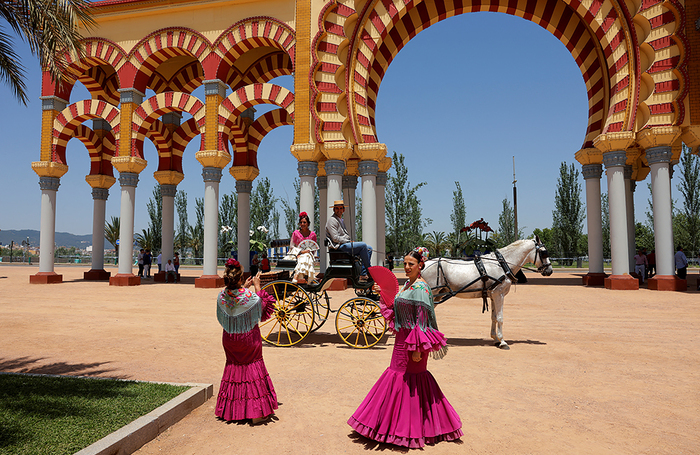 Женщины в традиционных платьях «севильяна» охлаждаются веерами в жаркий весенний день в Кордове, Испания.