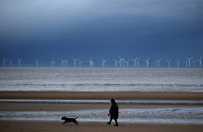 Женщина выгуливает собаку на пляже в курортном городе Нью-Брайтон. Западное побережье Великобритании.