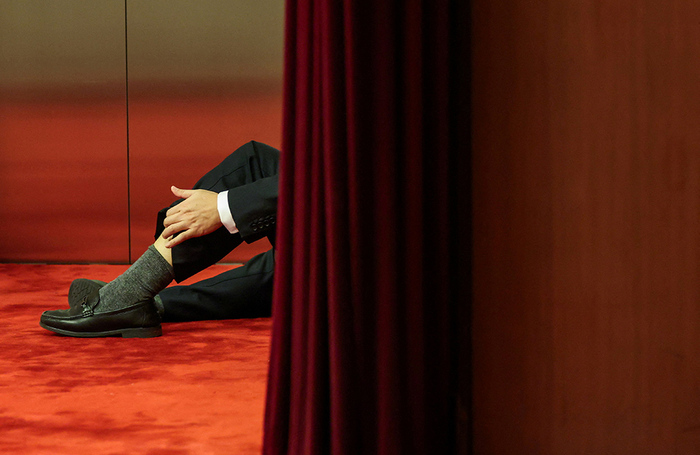 Мужчина сидит на красной ковровой дорожке в Большом зале народных собраний перед ежегодным заседанием Всекитайского собрания народных представителей в Пекине.