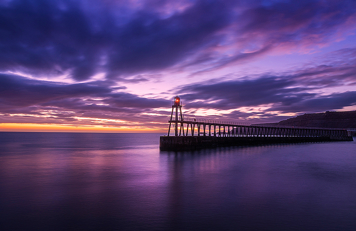 Восход солнца в Уитби на побережье Йоркшира над маяком Ист-Пир.