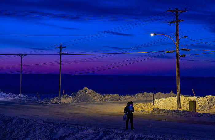 Человек идет по улице на закате в Кембридж-Бей в Канаде.