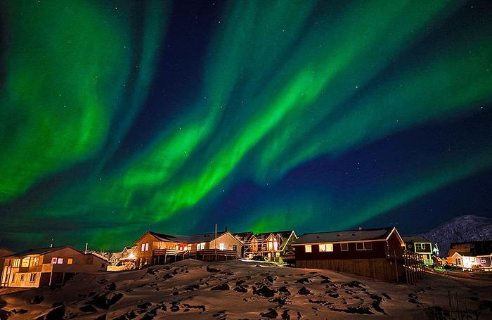 Северное сияние освещает небо над домами в Нууке, Гренландия.