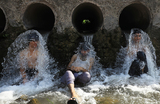 Люди охлаждаются водой из водопроводных труб в жаркую погоду на окраине Пешавара, Пакистан.