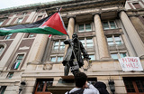 Участник студенческого митинга в поддержку палестинцев с флагом Палестины в руках возле входа в Гамильтон-холл в кампусе Колумбийского университета, где сосредоточился центр протестов. Десятки студентов захватили и забаррикадировались в Гамильтон-Холле, который протестующие окрестили «Хинд-холлом» (Hind’s Hall), выразив таким образом  дань уважения Хинд Раджаб, шестилетней палестинской девочке, погибшей в секторе Газа в войне Израиля против ХАМАС. Последний раз здание Гамильтон-Холла было захвачено студентами в 1968 году во время протестов против расовой сегрегации и войны во Вьетнаме. Нью-Йорк, США.