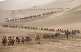 Туристы, катающиеся на верблюдах, посещают песчаные дюны в Дуньхуане, провинция Ганьсу. Китай. 