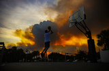 Мужчина играет в баскетбол в парке Doral Legacy Park, в то время как лесной пожар бушует относительно недалеко от жилого района Дорал в Майами.